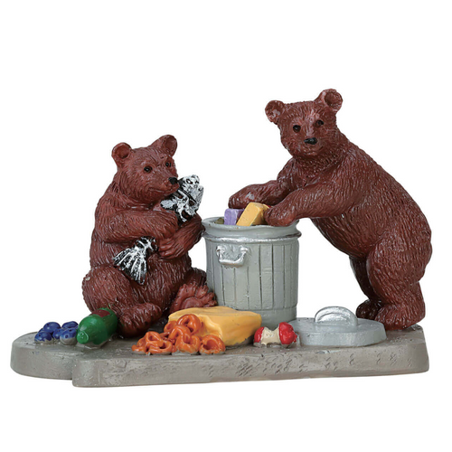 Two bear figurines around a trash can with food items on a white background