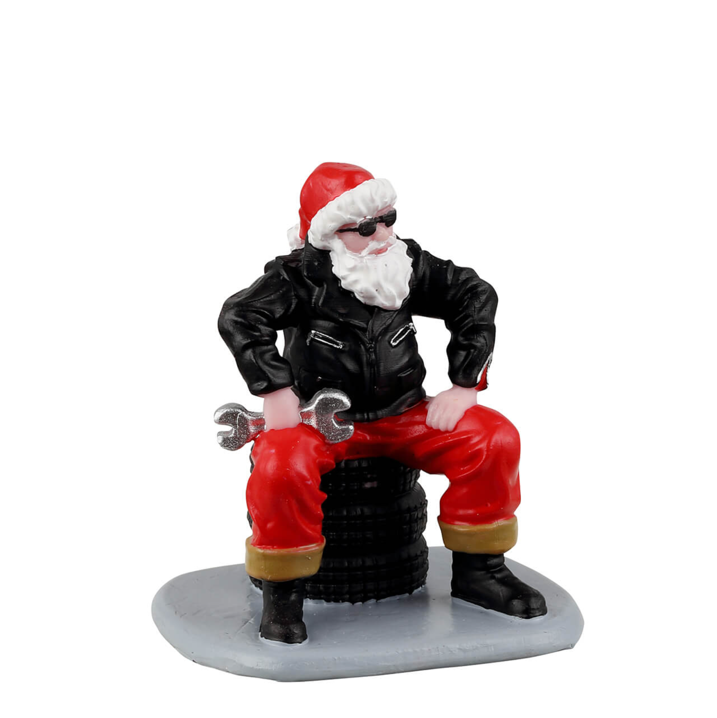 Figurine of a Santa Claus character in a leather jacket and red pants sitting on a tire with a wrench, on a white background.